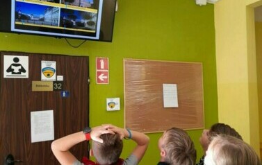 Uczniowie ogladają infromacje na korytarzu wyświetlone na telewizorze. 