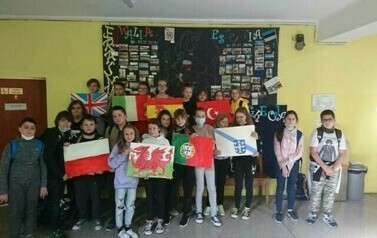 Wspólne zdjęcie uczniów w szkole z flagami państw Erazmus.